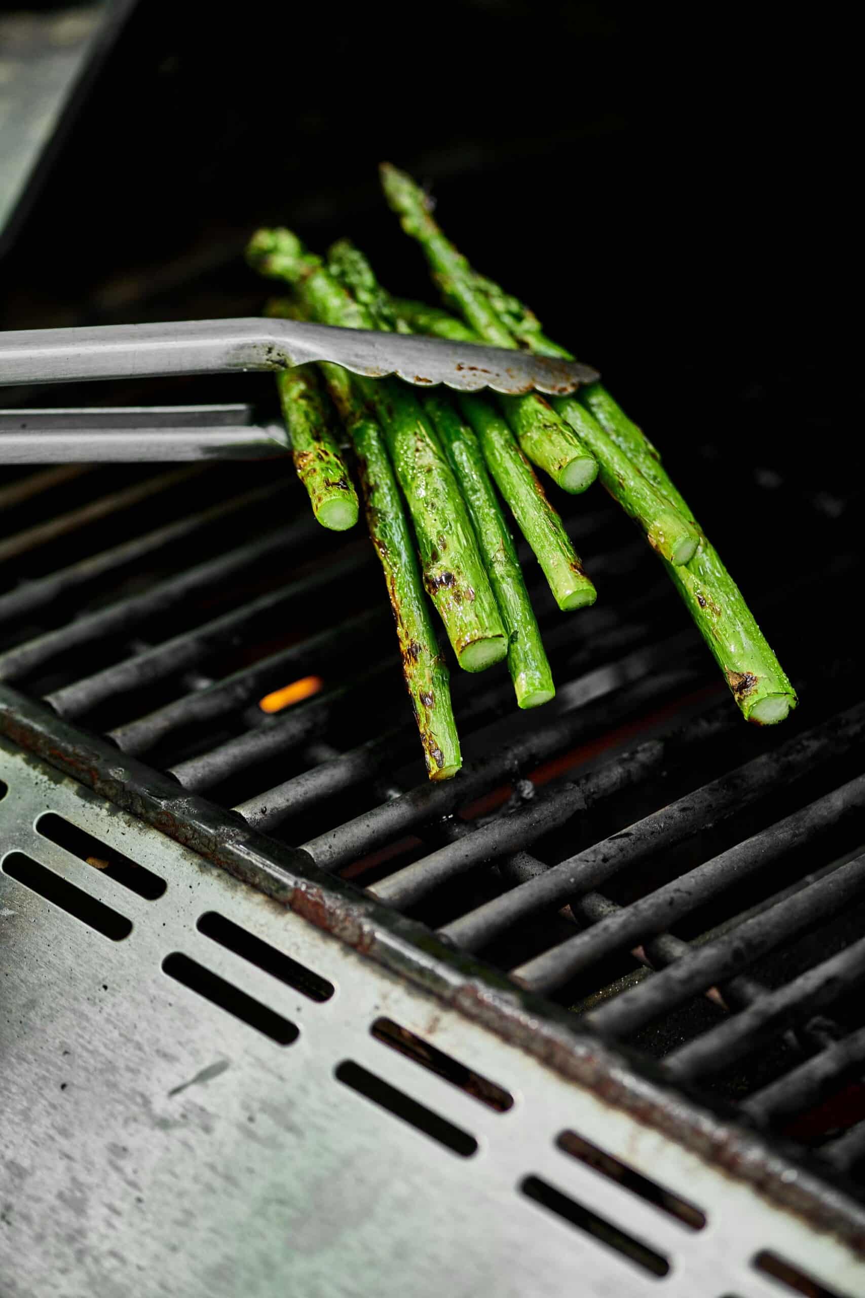 Tongs grabbing asparagus from a grill.