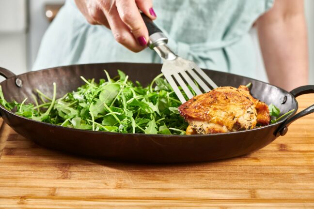Woman placing a Lemon Garlic Chicken Thigh onto a plate with greens.