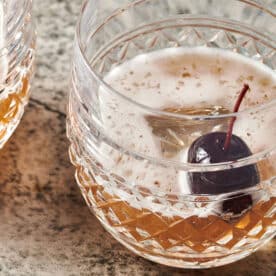 Two Manhattan cocktails garnished with cherries in glasses.