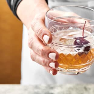 Woman holding a Manhattan Cocktail in a rocks glass.