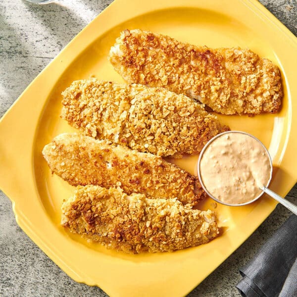 Tilapia crusted with crushed tortilla chips on yellow platter with sriracha mayo.