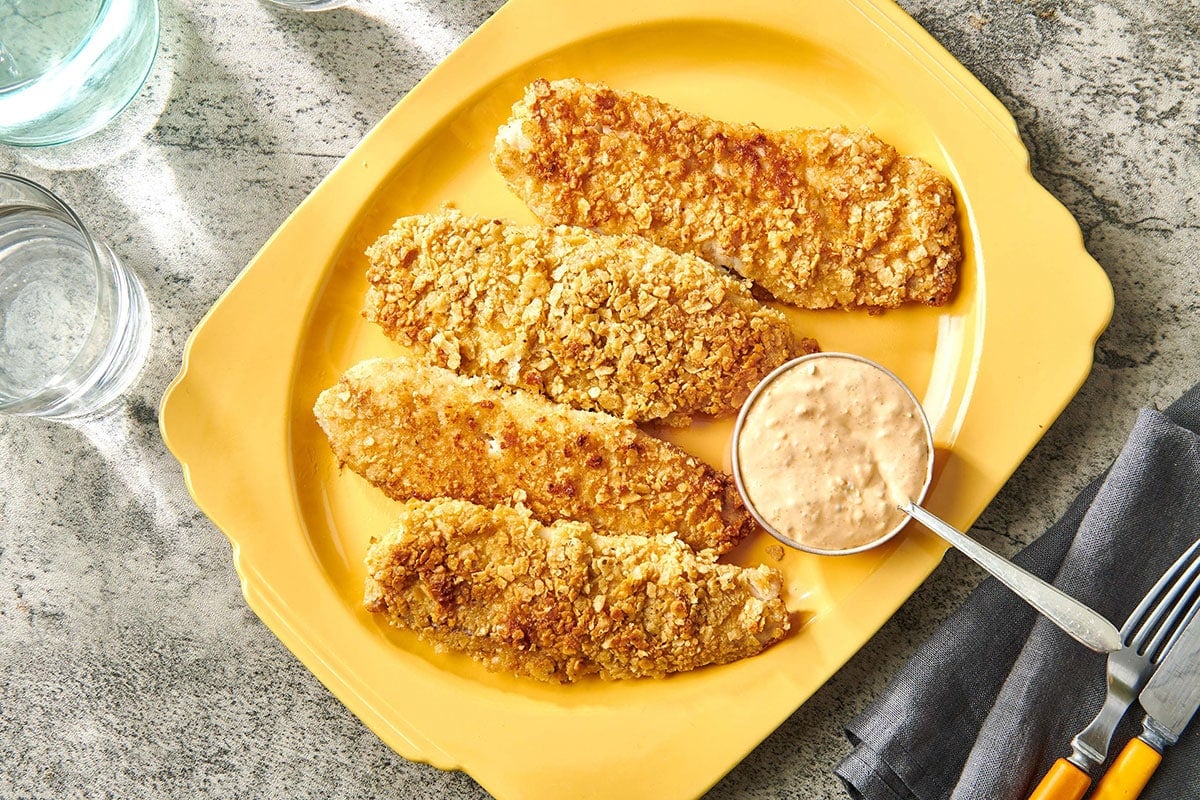 Tilapia crusted with crushed tortilla chips on yellow platter with sriracha mayo.