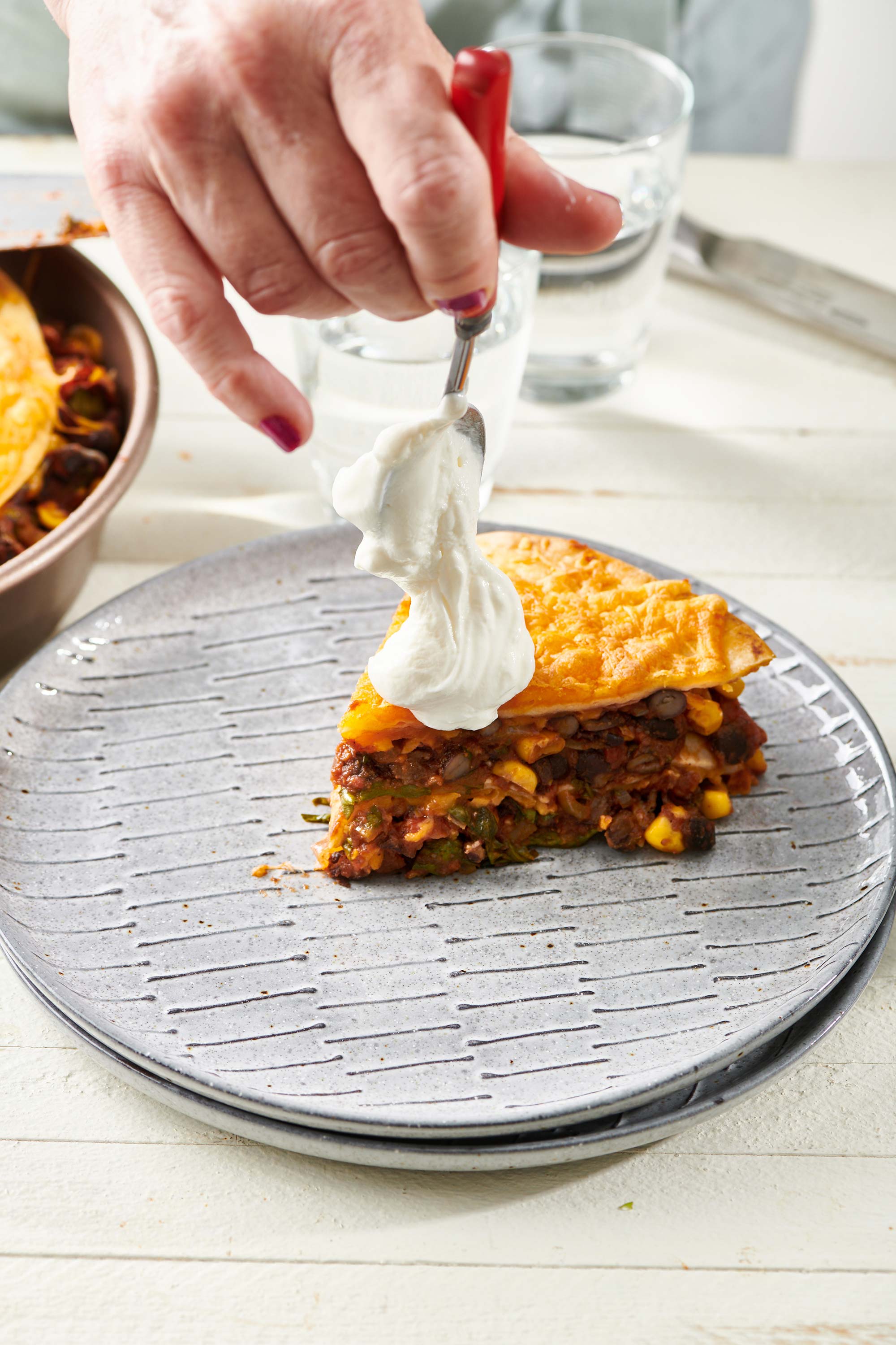 Spoon putting a dollop of sour cream on a slice of Vegetarian Mexican Lasagna.
