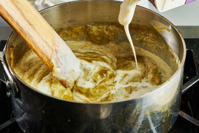 Cream pouring into a pot of asparagus soup.