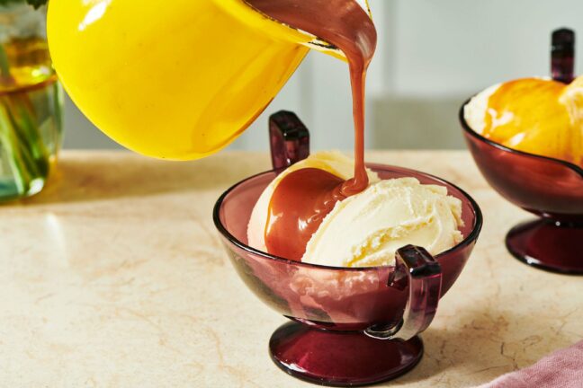 Yellow pitcher of Caramel Sauce pouring over ice cream.
