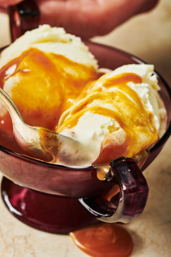 Spoon in a bowl of ice cream covered in caramel sauce.