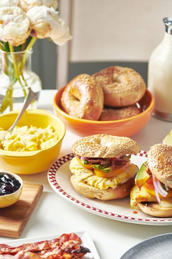 Two breakfast sandwiches on a plate on a table set with breakfast ingredients.