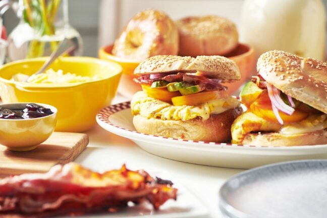 Breakfast sandwiches, bagels, eggs, bacons, and other ingredients on a table.