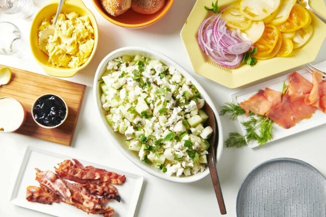 Table set with plates and bowls on ingredients including eggs, bacon, and red onion.