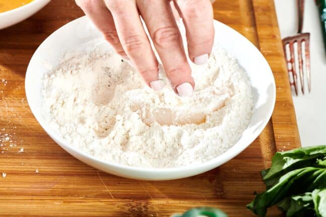 Woman dipping fish in a flour mixture.