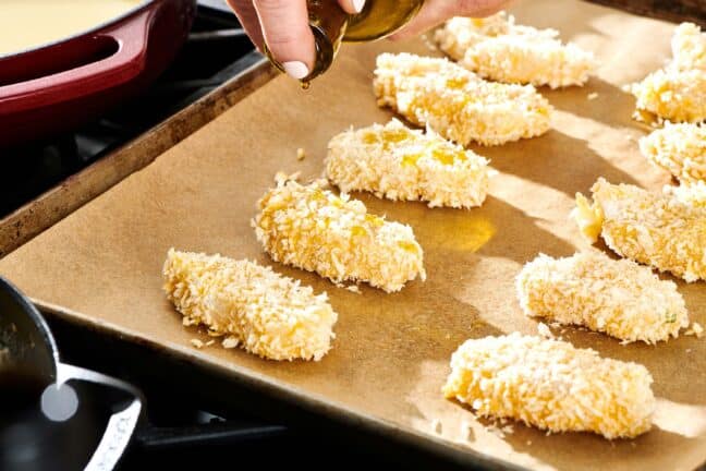 Woman drizzling olive oil on a baking sheet of breaded fish.