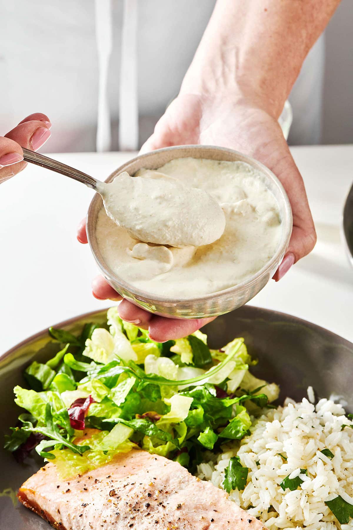 Woman holding a spoon and bowl of Horseradish Sauce over a plate.