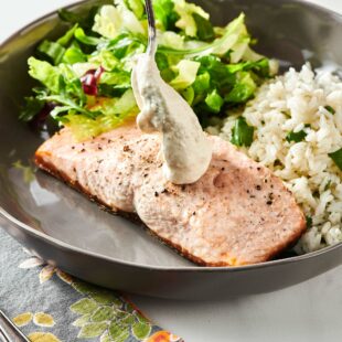 Spoon adding Horseradish Sauce to salmon on a plate with rice and salad.