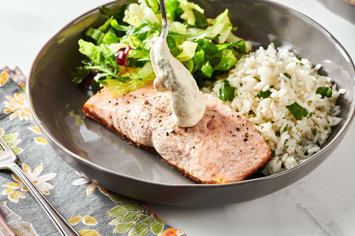Spoon adding Horseradish Sauce to salmon on a plate with rice and salad.