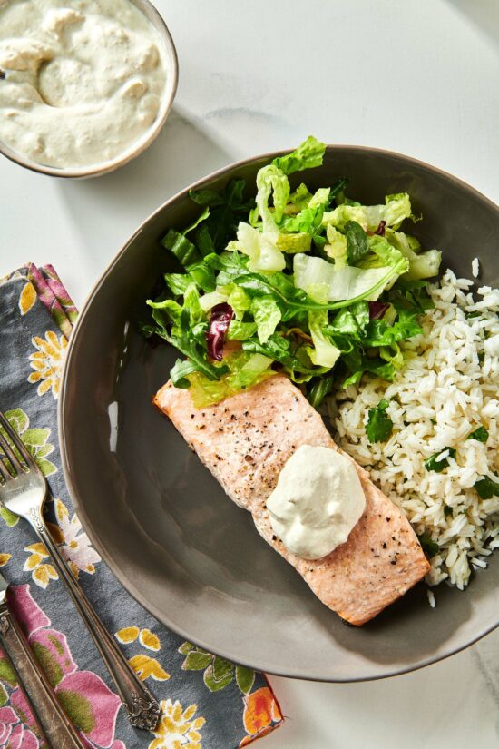 Salmon topped with Horseradish Sauce on a dark plate with salad and rice.