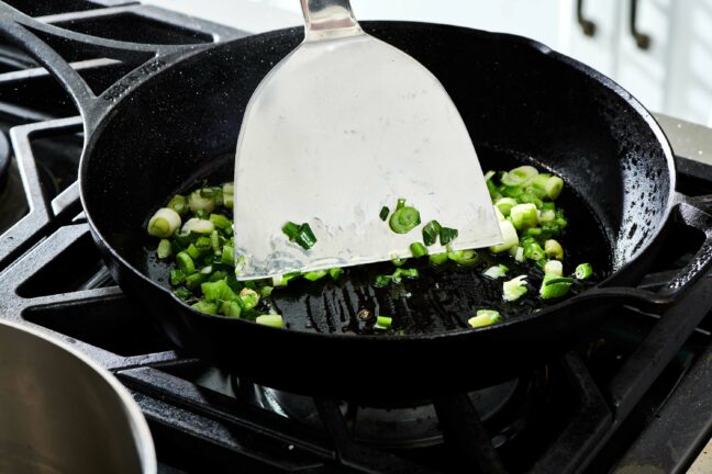 Metal spatula in a skillet of chopped scallions.