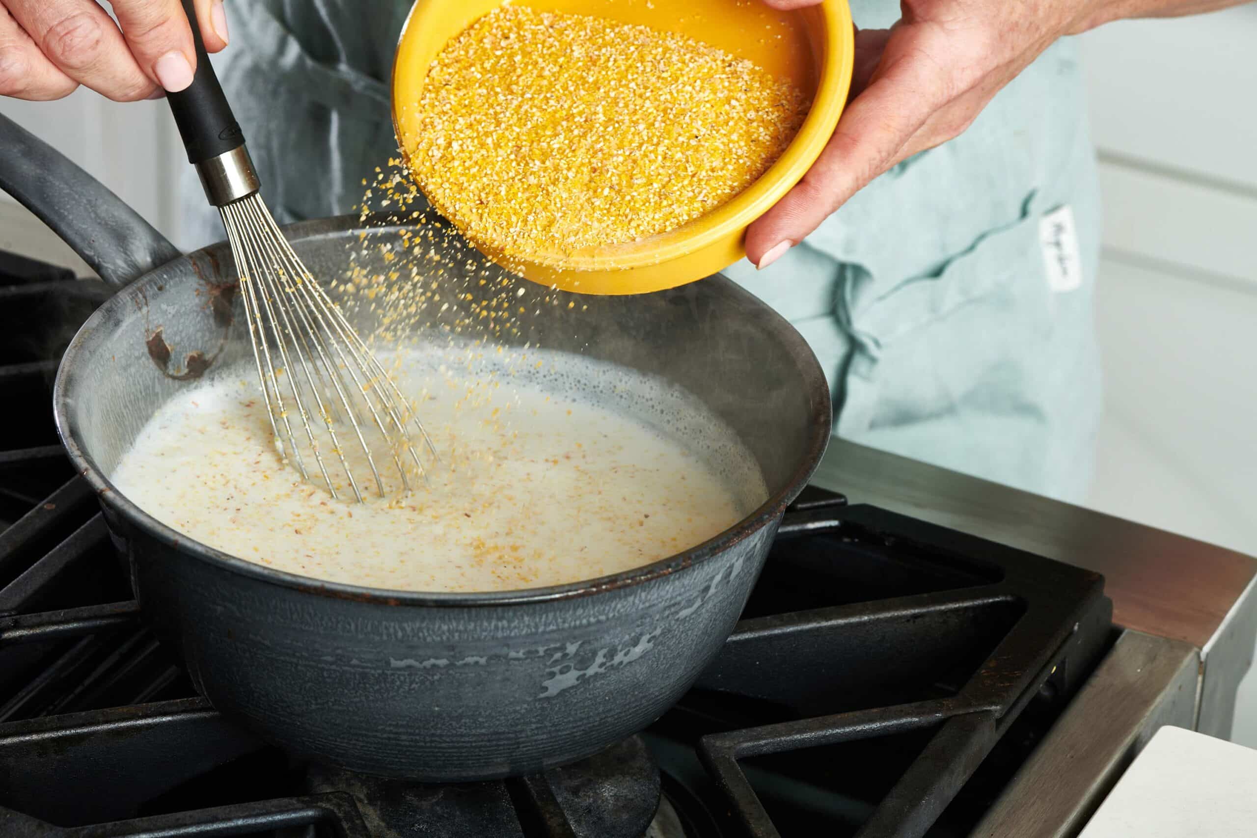 Yellow bowl pouring grits into a pan of milk mixture.