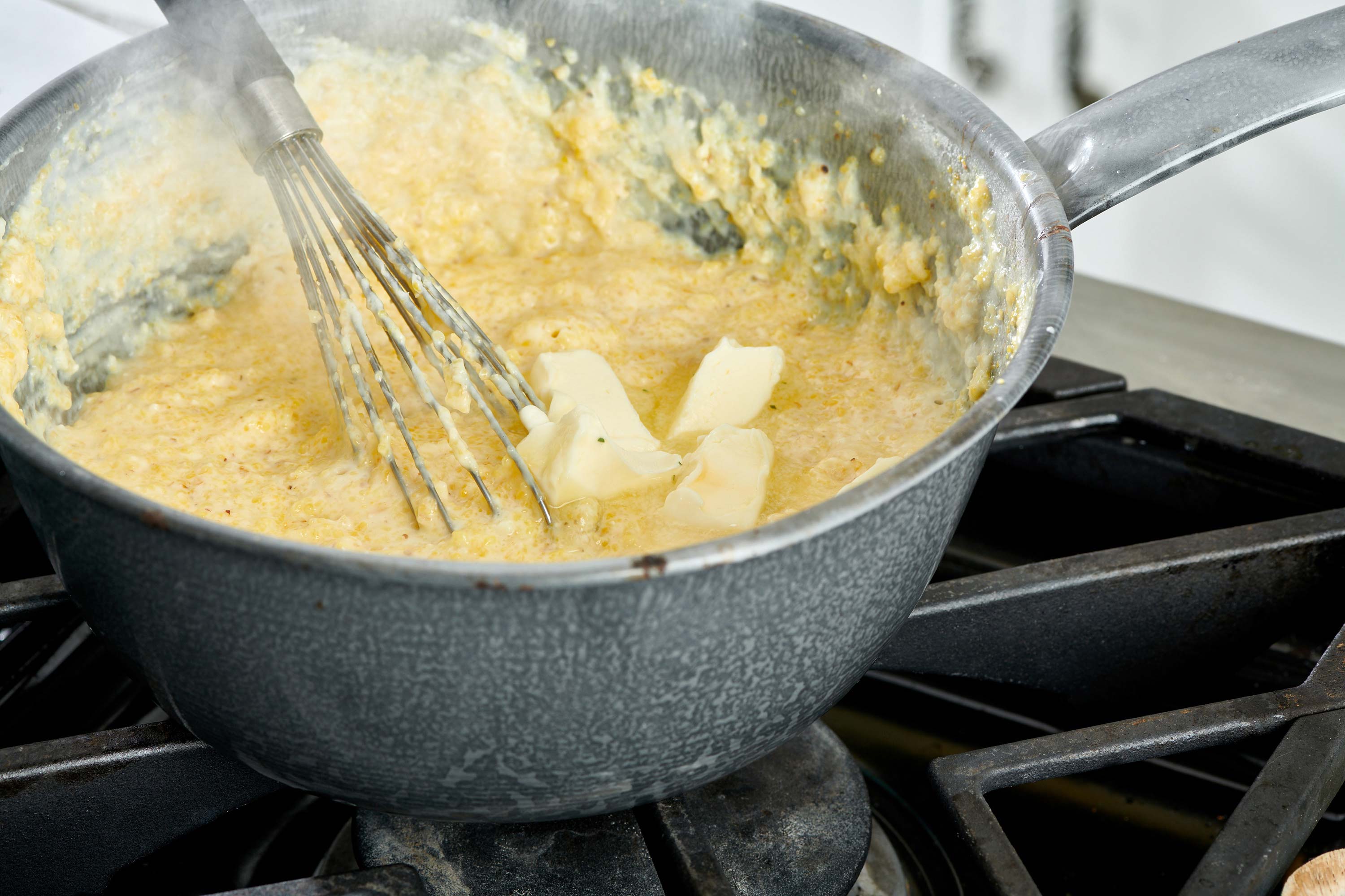 Chunks of butter in a pan of grits with a whisk.