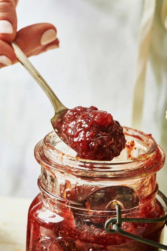 Spoon of strawberry jam over a jar.