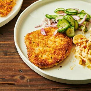 Pork Schnitzel on a plate with cucumber salad and potato.