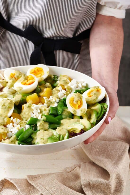 Woman holding a bowl of Spring Cobb Salad with Scallion Dressing.