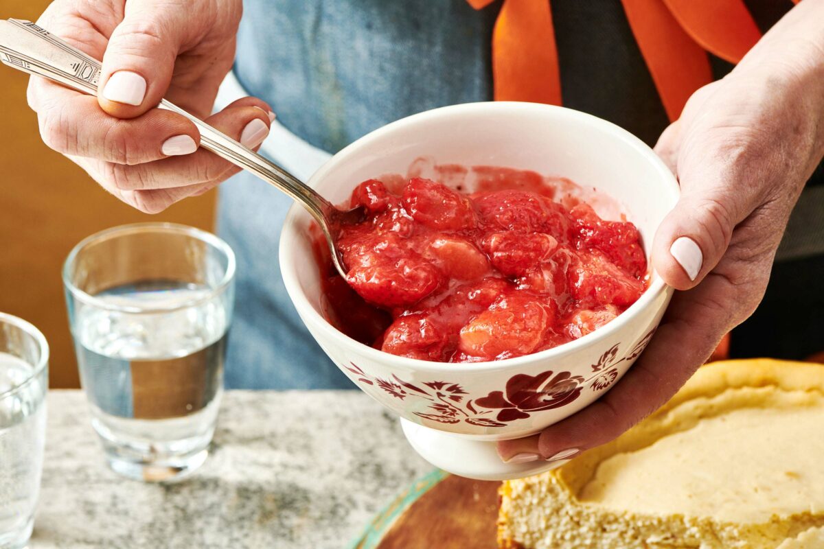 Woman scooping strawberry topping from a small bowl.