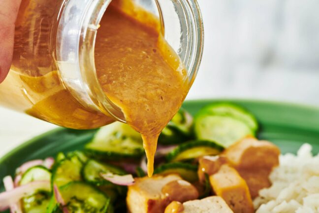 Peanut sauce pouring from a jar onto tofu.