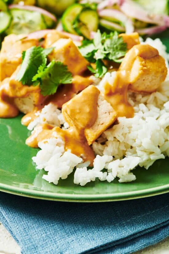 Tofu with Peanut Sauce on a bed of rice on a green plate.