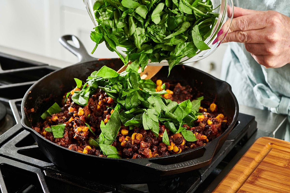 Pouring chopped spinach into a skillet of Vegetarian Mexican Lasagna filling.