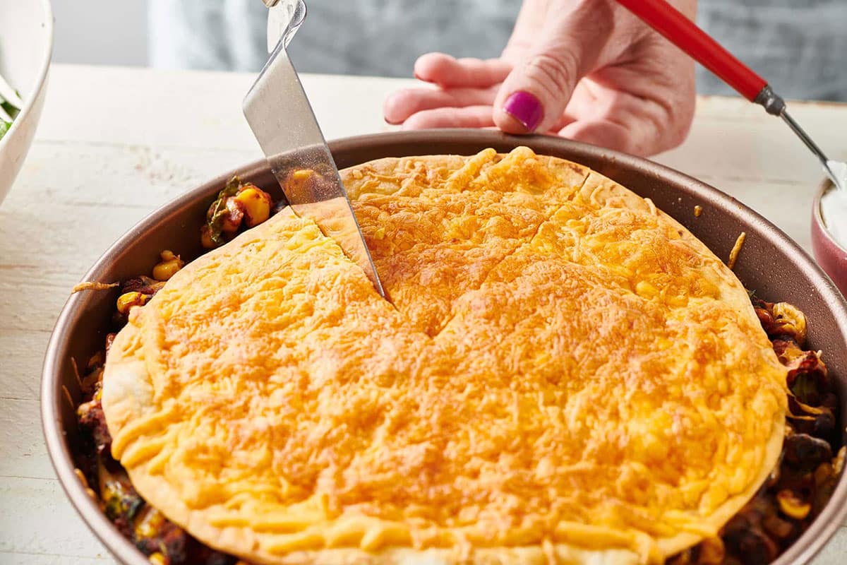 Slicing Vegetarian Mexican Lasagna in baking pan.