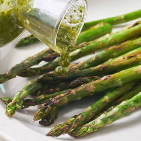 Pouring scallion chimichurri sauce over grilled asparagus on plate.