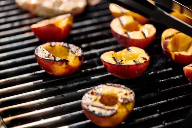 Peach halves with grill marks on a grill.