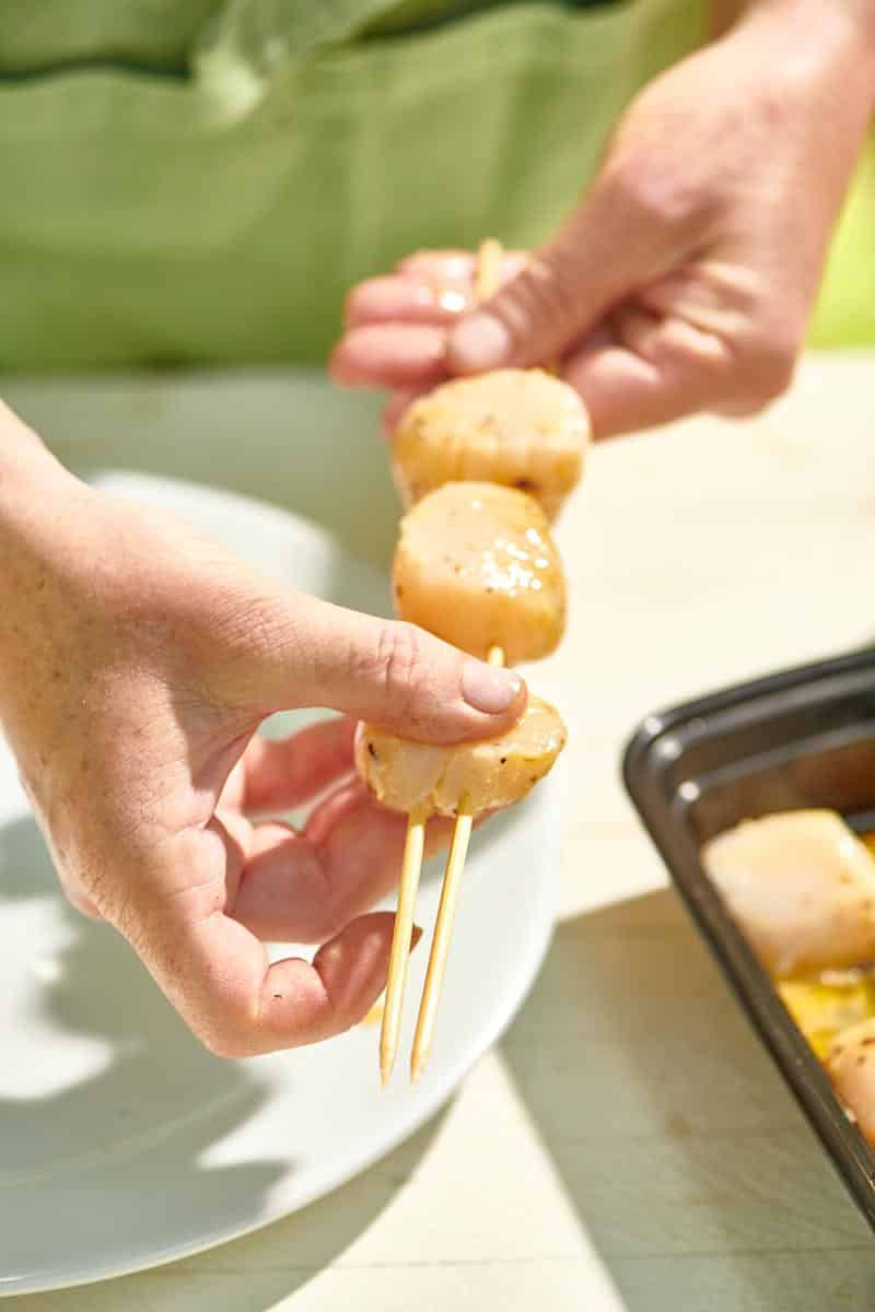 Woman adding another scallops to skewers.