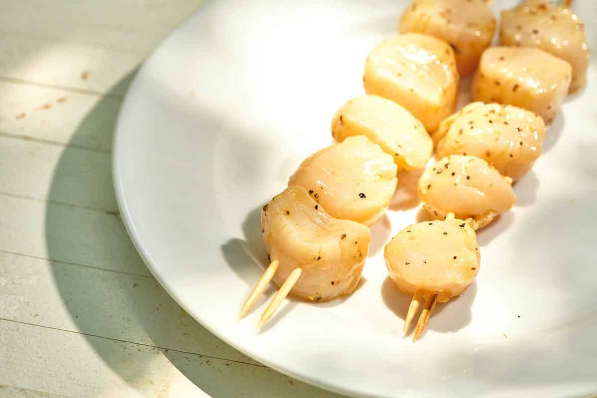 Skewered scallops on white plate.