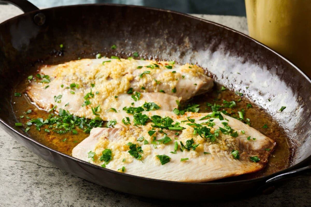 Two lemon garlic tilapia filets in frying pan on counter.