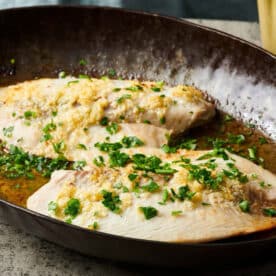 Two lemon garlic tilapia filets in frying pan on counter.