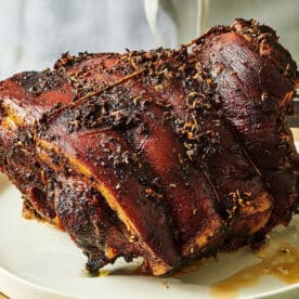 Porchetta on a white plate next to a knife.