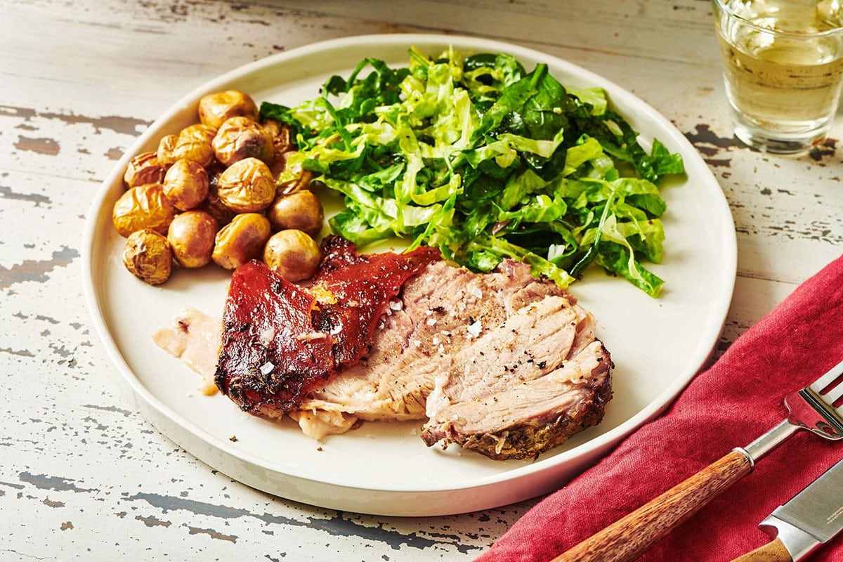 Sliced Porchetta, salad, and potatoes on a white plate.