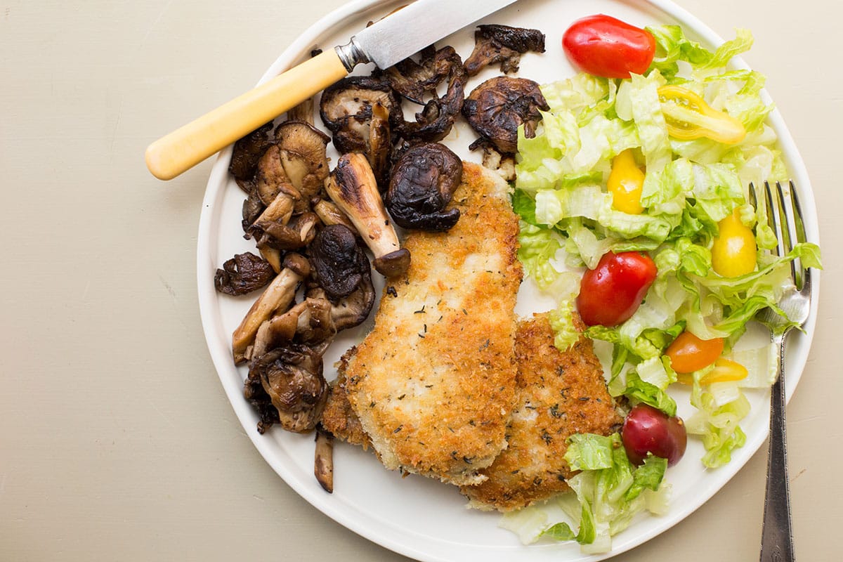 Knife on a plate with salad and Pork Schnitzel with Sautéed Mushrooms.