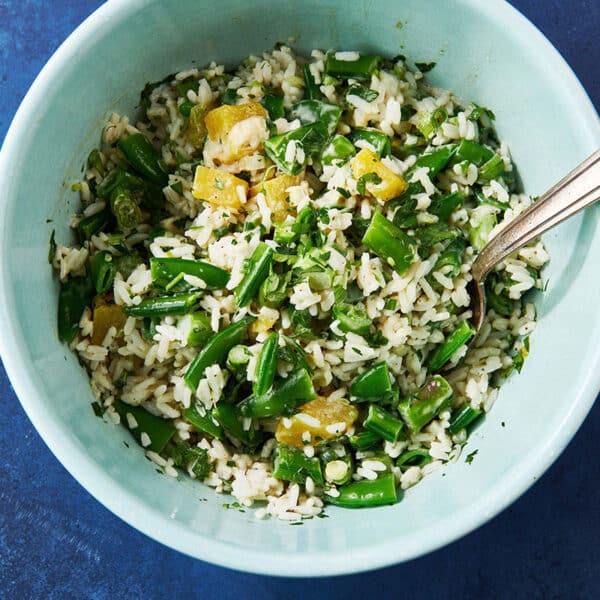 Rice and vegetable salad in bowl with spoon on blue table.