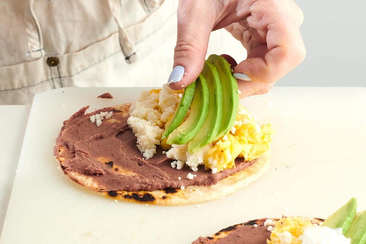 Woman placing avocado slices onto a Baleada.