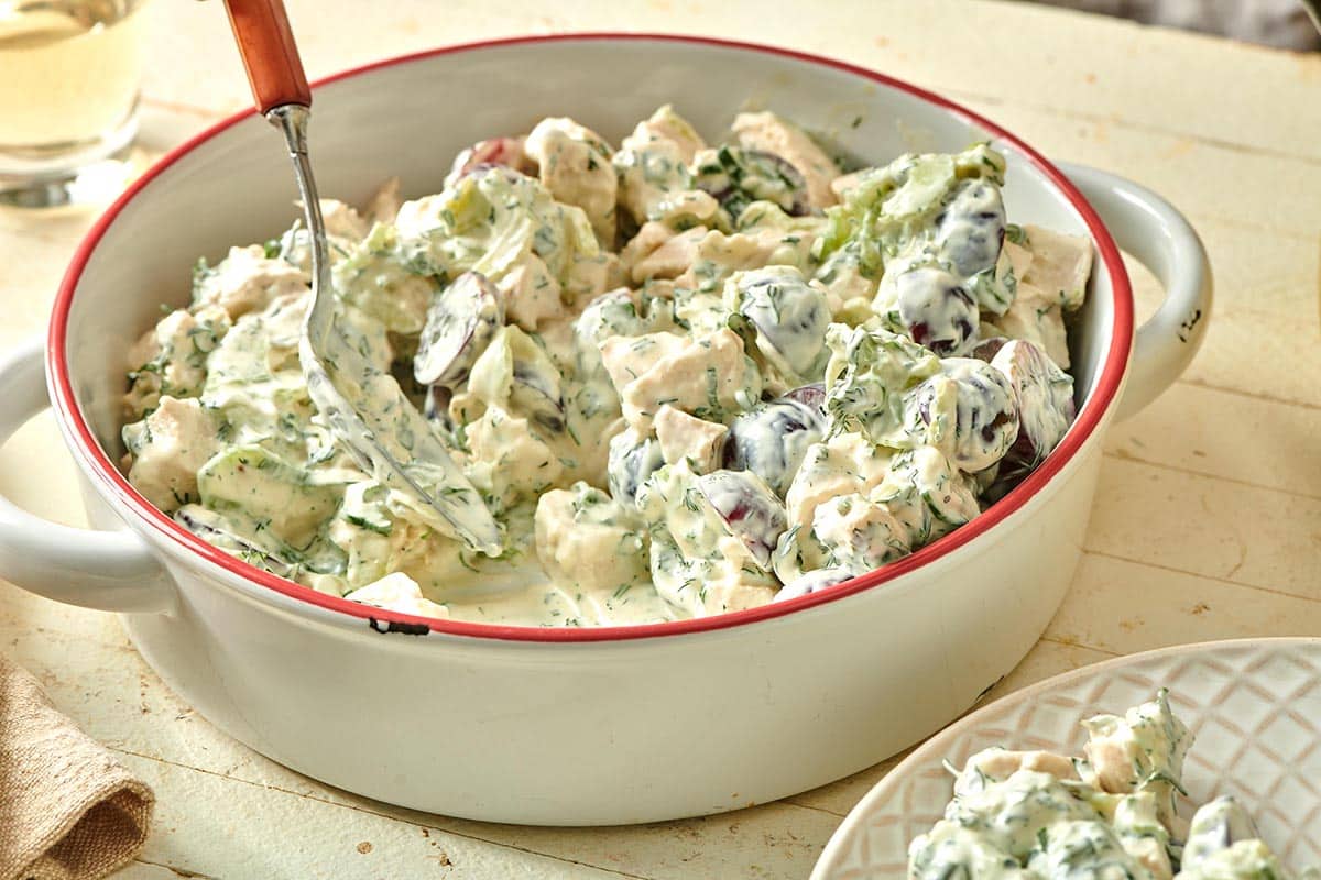 Spooning Chicken Salad with Grapes out of white serving dish.