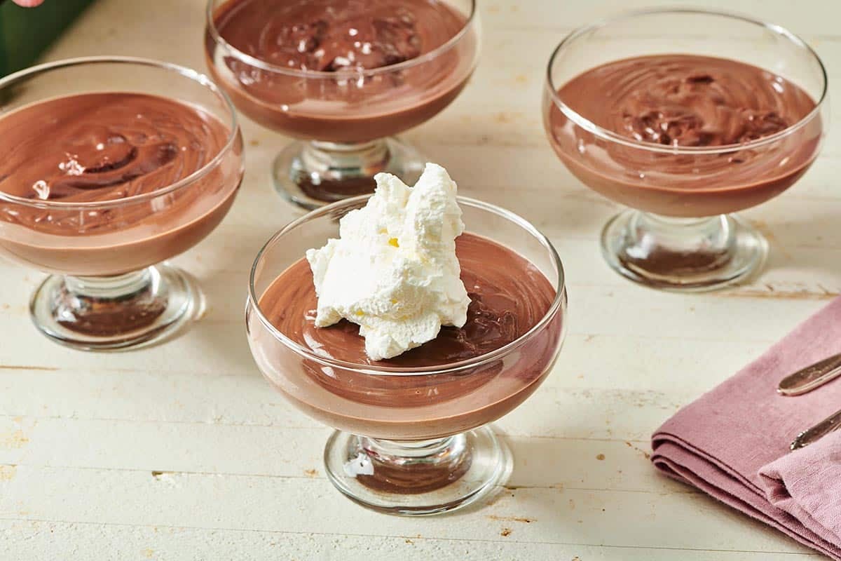 Several large serving glasses of Chocolate Pudding, one of which is topped with whipped cream.