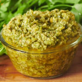 Green olive tapenade in glass bowl on table with herbs.