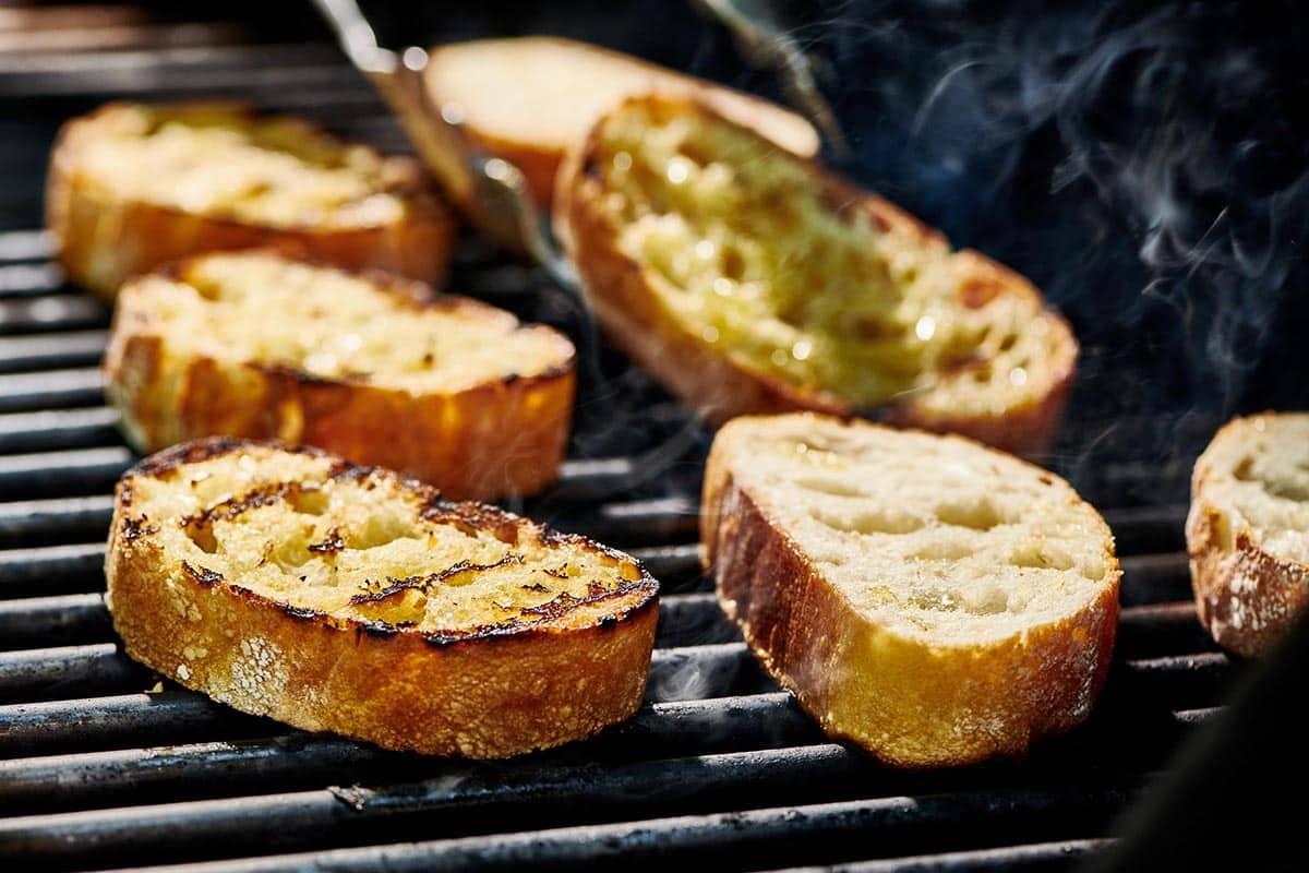 Tongs grabbing a slice of bread on a grill.