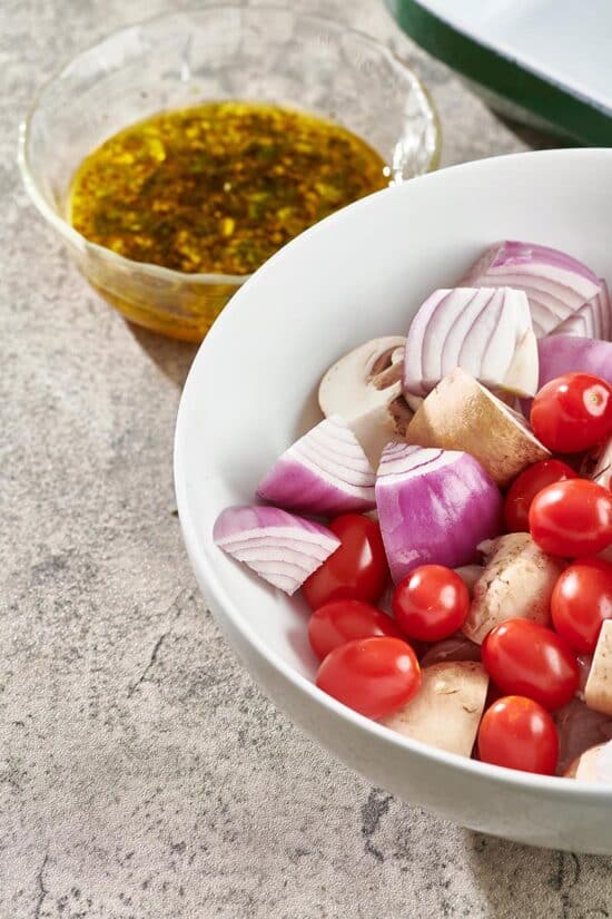 White bowl of red onion, mushrooms, and tomatoes.