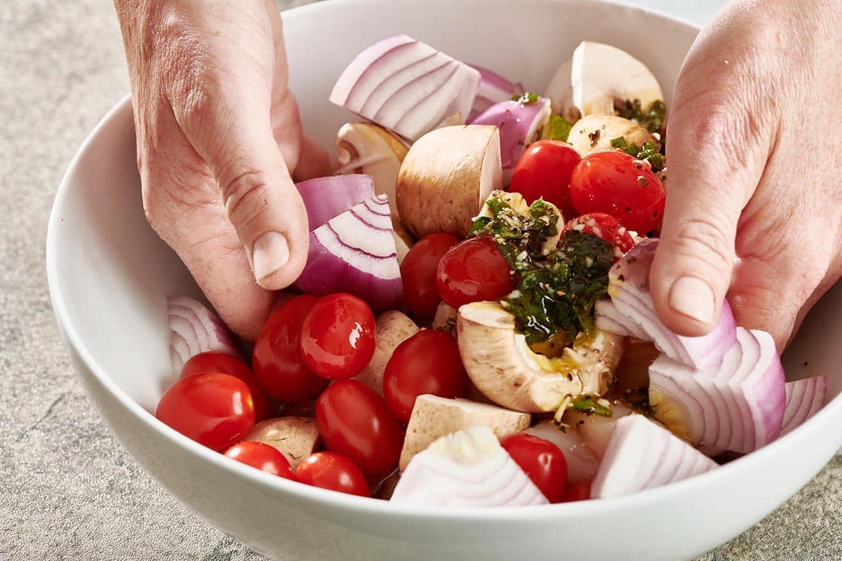 Woman tossing vegetables with citrus-basil marinade.