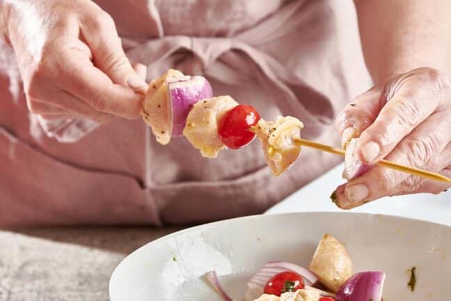 Woman placing a hunk of red onion onto a skewer.