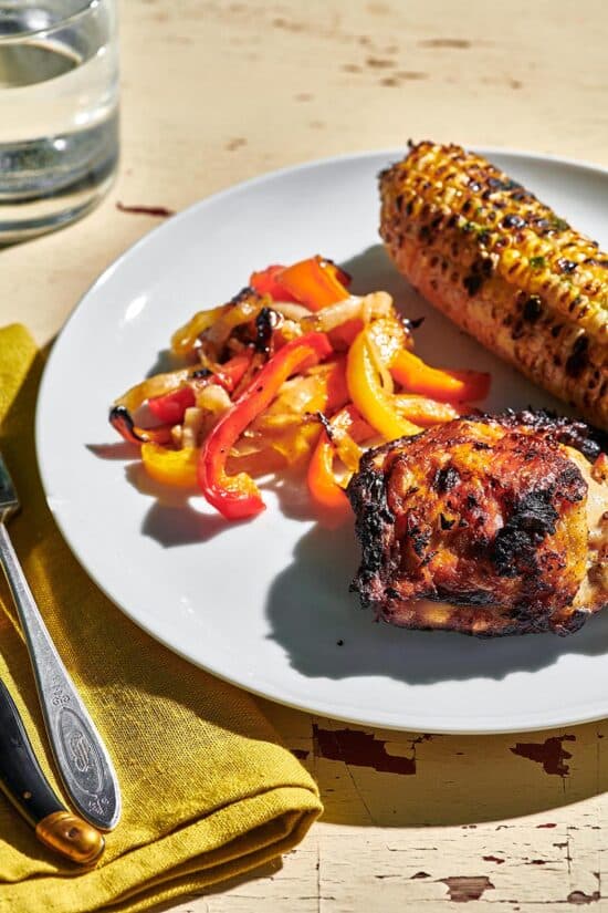 Grilled Chicken Thighs on a plate with corn and peppers.