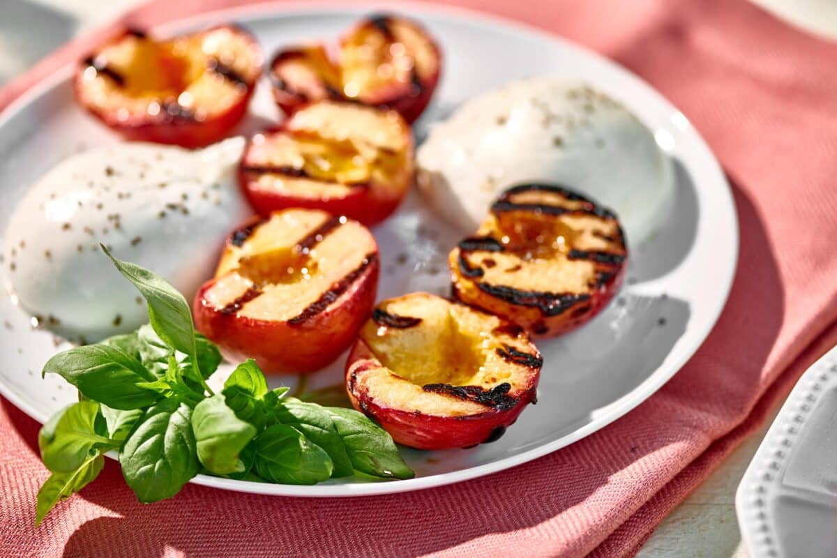 Grilled peaches on white plate with burrata cheese and fresh basil.